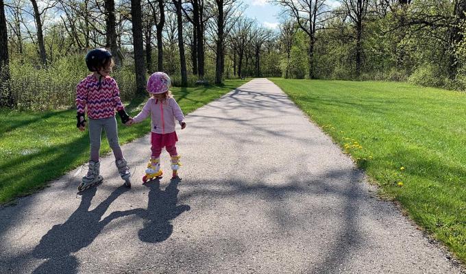 Photo of two little girls holding hands and skating on a path
