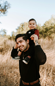 Photo of a man carrying a toddler on his shoulders, both smiling