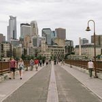 Photo of people walking across the Stone Arch Bridge with the Minneapolis skyline in the background