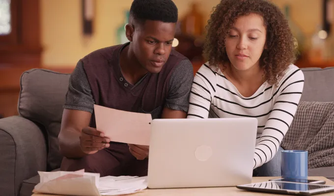 Photo of two young adults sitting on a couch, looking at papers and a laptop