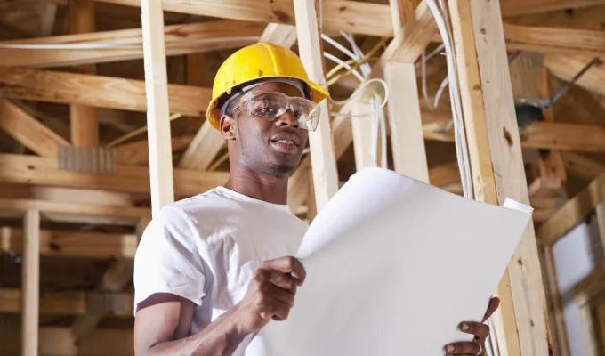 Photo of a man in a hard hat and safety glasses, reading a plan