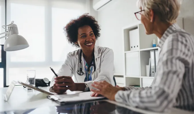 Photo of a smiling health care provider, sitting at a table with her patient