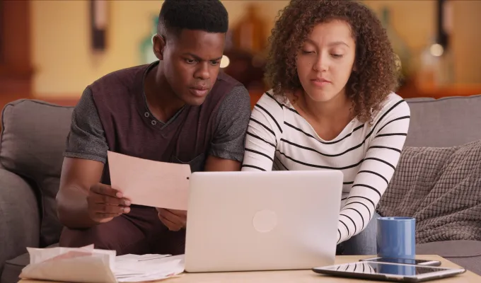 Photo of two young adults sitting on a couch, looking at papers and a laptop