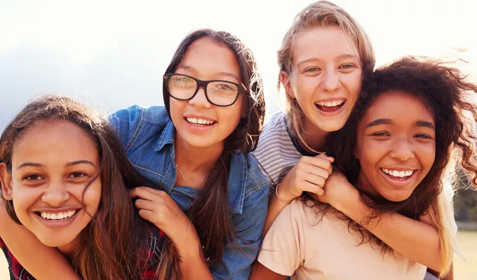 Photo of four girls smiling, grouped tightly with arms around each other