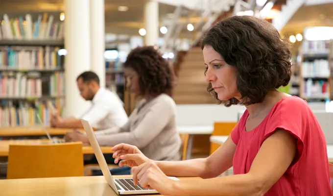 Photo of three adults working at laptops in a library