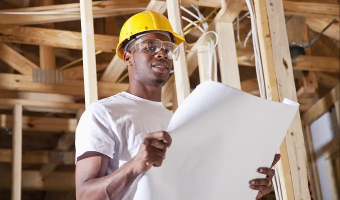 Photo of a man in a hard hat and safety glasses, reading a plan