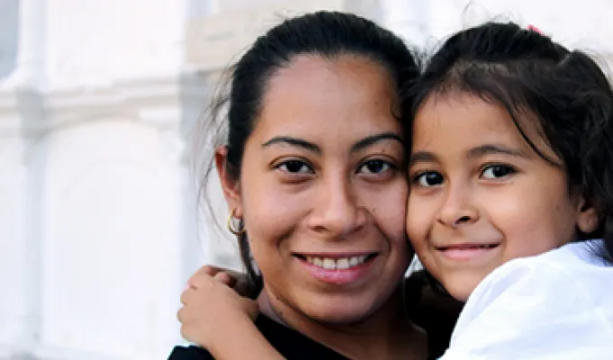Photo of a woman and child hugging, smiling, and looking directly at the camera