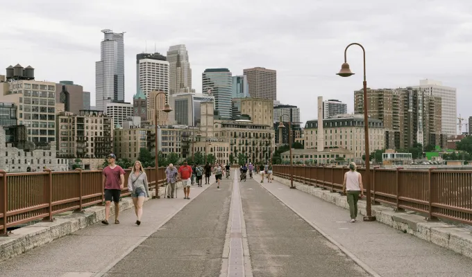 Photo of people walking across the Stone Arch Bridge with downtown Minneapolis in the background