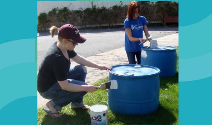 Photo of two young woman painting barrels for a community project