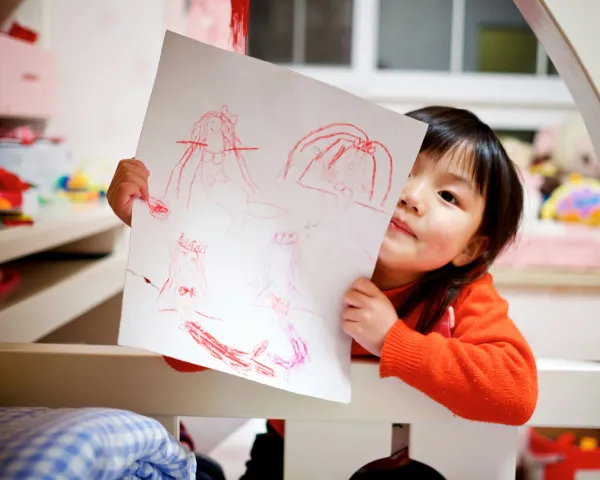 Photo of a young girl showing off a picture she drew. Her bedroom is in the background. Photo of Jerry Wang on Unsplash