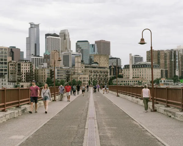 Photo of people walking across the Stone Arch Bridge with the Minneapolis skyline in the background