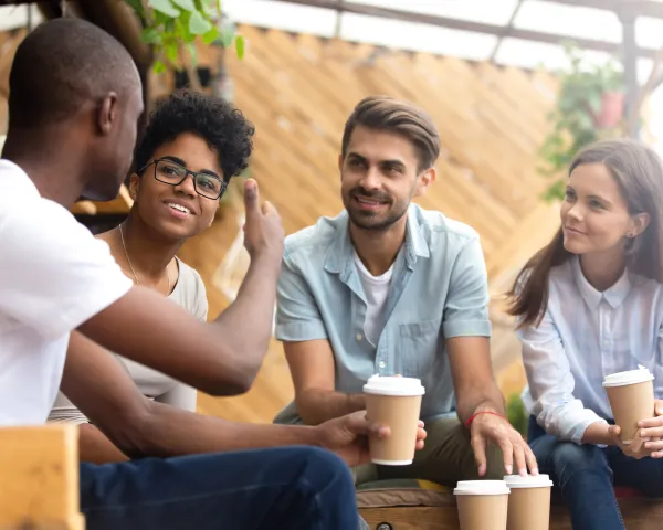 Photo of four young adults sitting on benches and having coffee