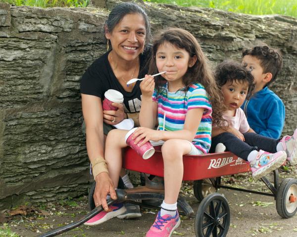Photo of Latino family - a mom with three young children who are in a red wagon.
