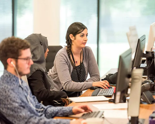 Photo of a woman working on a computer, with two colleagues working at nearby computers
