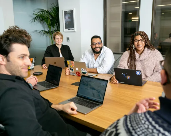 Photo of adults sitting around a board table, smiling, with laptops in front of them