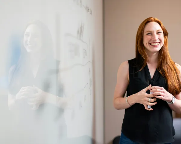 Photo of a young woman standing and smiling in front of a white board