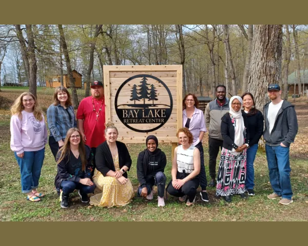 Photo of the 2024 Initiators Fellows standing around a sign that says Bay Lake Retreat Center. Photo courtesy of the Initiative Foundation.