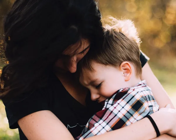 Photo of young mother cuddling her young son. Photo by Jordan Whitt on Unsplash