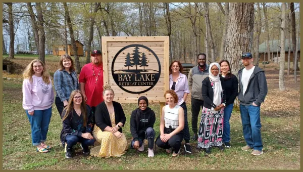 Photo of the 2024 Initiators Fellows standing around a sign that says Bay Lake Retreat Center