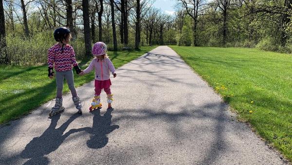 Two little girls roller skating down a trail