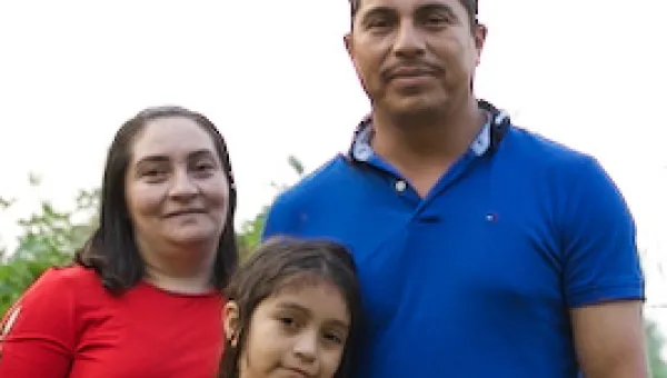 Photo of a Latino Minnesotan family: dad, mom, an elementary-school daughter and a pre-school son. There are orange flowers, trees, and a river in the background.