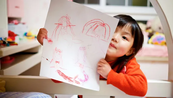 Photo of a young girl showing off a picture she drew. Her bedroom is in the background. Photo of Jerry Wang on Unsplash