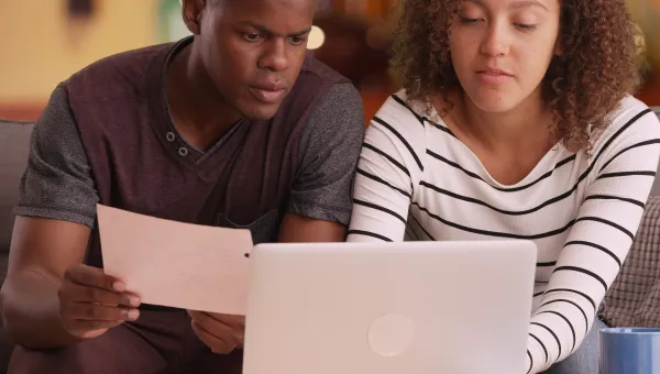 Photo of two young adults sitting on a couch, looking at papers and a laptop