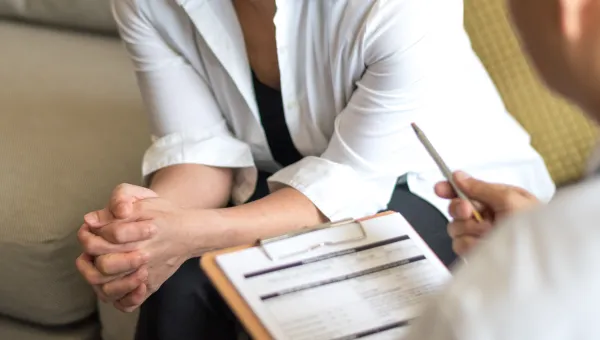 Cropped photo of an adult, sitting with another adult holding a clipboard