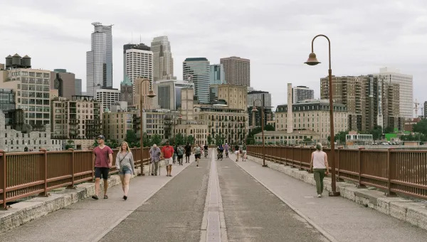 Photo of people walking across the Stone Arch Bridge with the Minneapolis skyline in the background