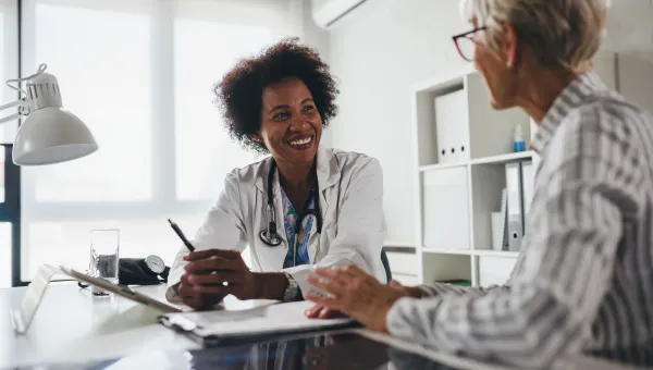Photo of a smiling health care provider, sitting at a table with her patient